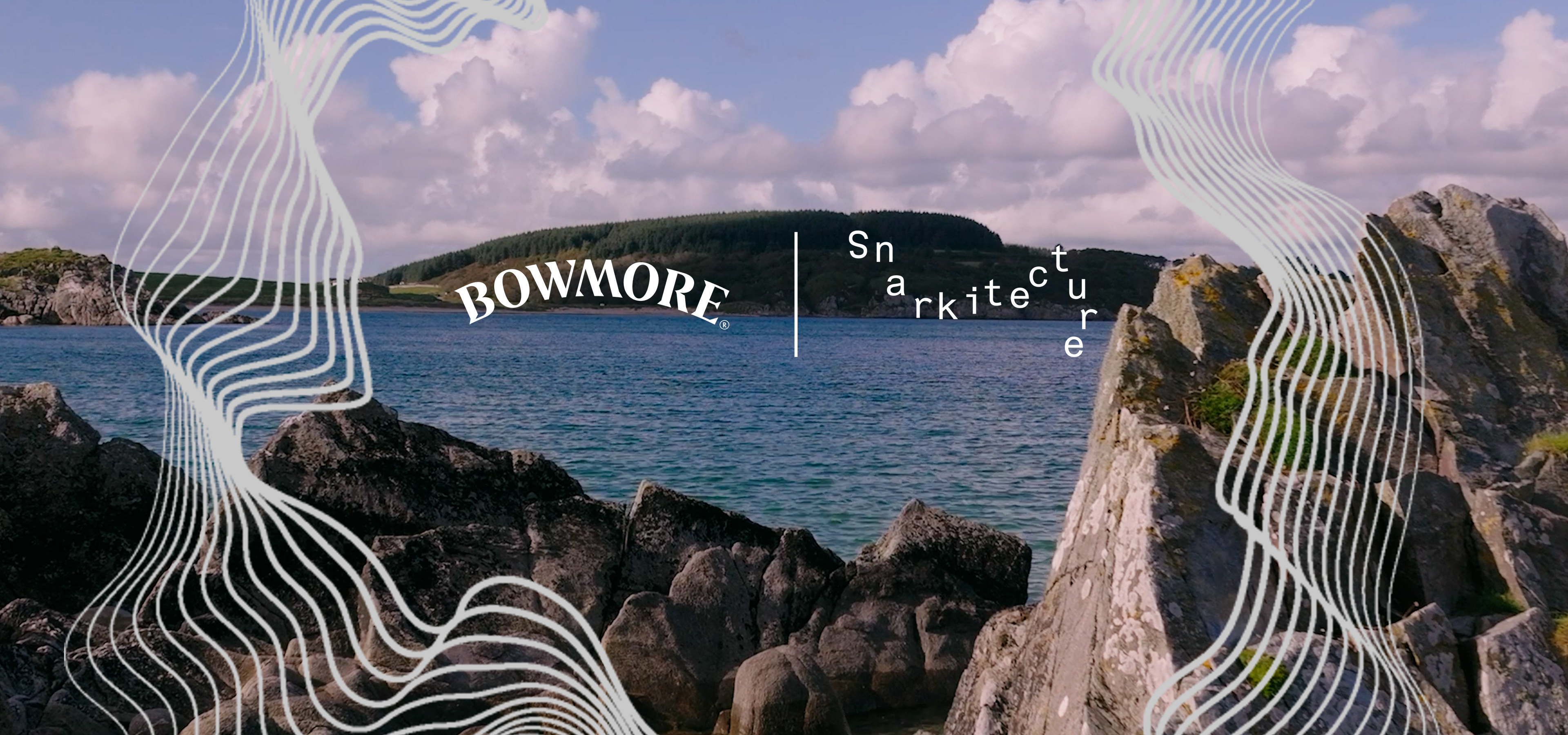 A rocky shoreline overlooks a calm bay with a tree-covered island in the distance beneath a blue sky with soft clouds. White flowing contour lines frame the top and bottom of the image, while the Bowmore and Snarkitecture logos appear near the center, highlighting the collaboration against the coastal Islay landscape.