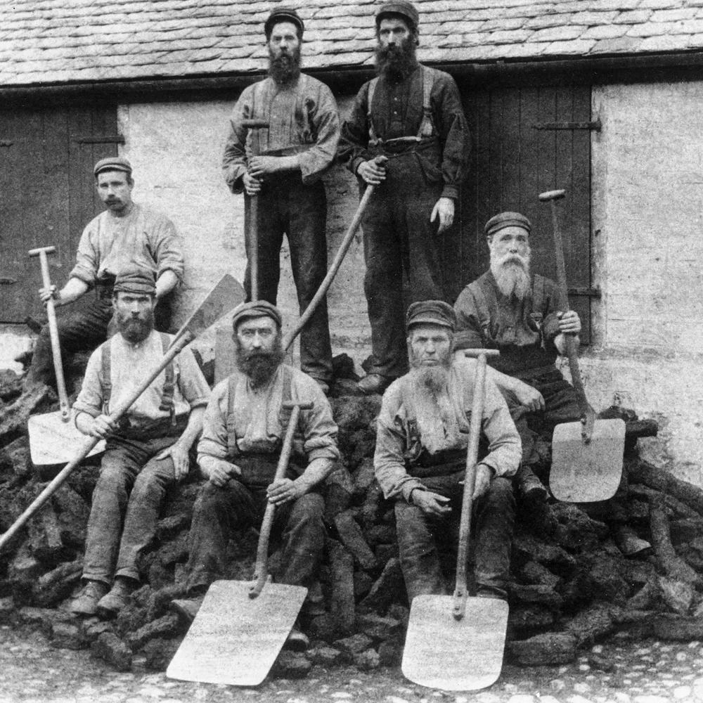 Seven bearded men with shovels on peat-mound.