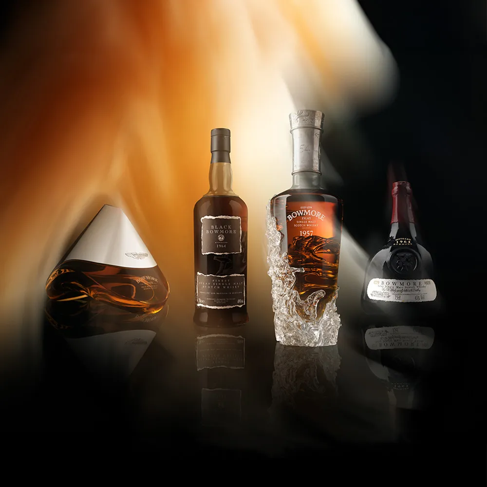 Four premium Bowmore bottles on reflective surface.