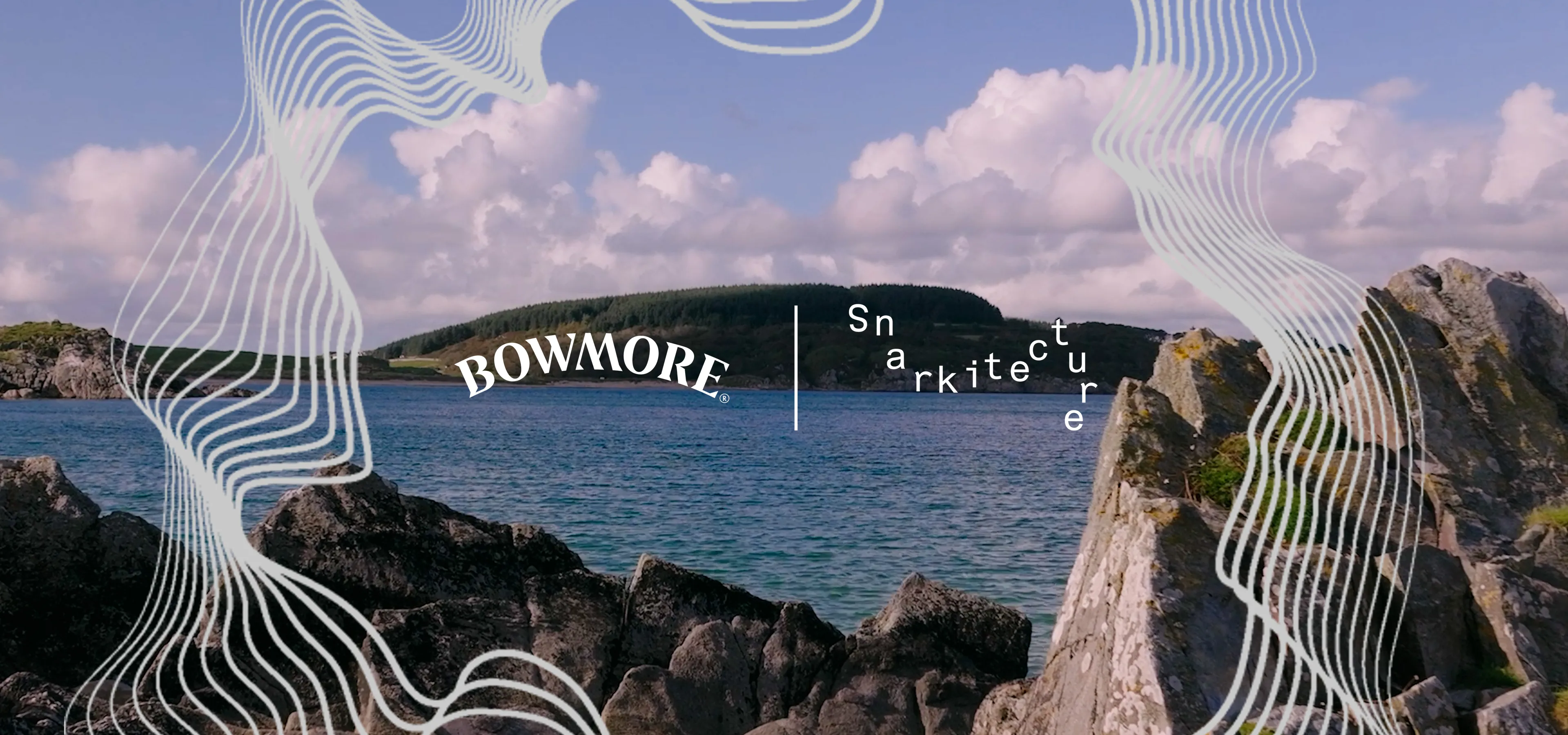 A rocky coastal shoreline frames a calm bay with a forested island under a blue sky filled with fluffy clouds. White wavy line graphics form an abstract border around the image. Centered over the landscape are the Bowmore logo, a vertical divider, and a stylized "Snarkitecture" logo, suggesting a collaboration between the two brands.