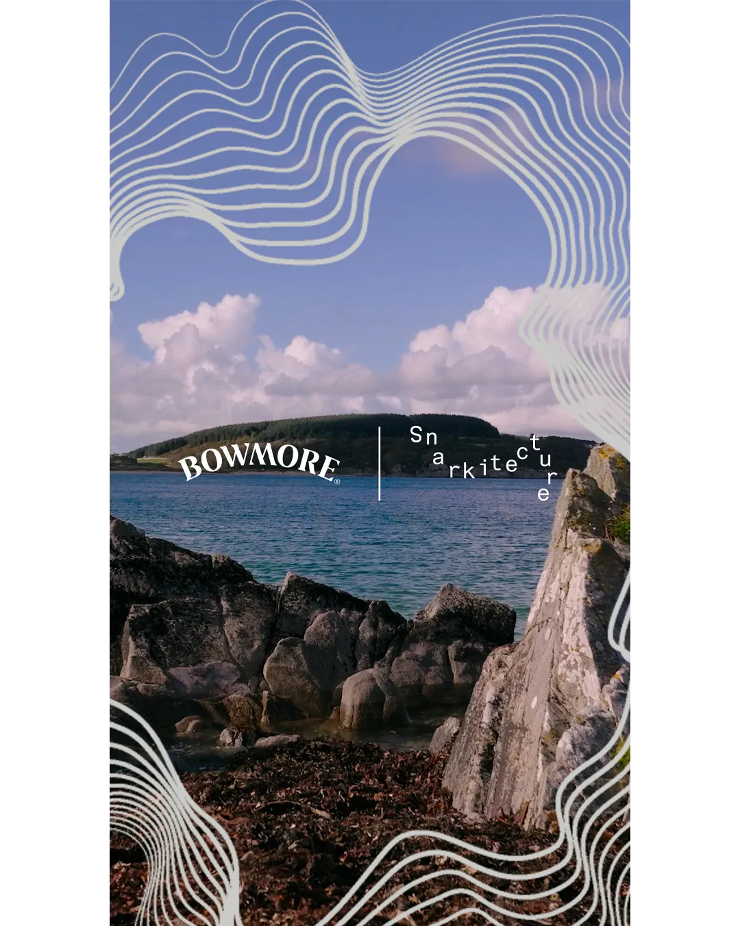 A rocky shoreline overlooks a calm bay with a tree-covered island in the distance beneath a blue sky with soft clouds. White flowing contour lines frame the top and bottom of the image, while the Bowmore and Snarkitecture logos appear near the center, highlighting the collaboration against the coastal Islay landscape.